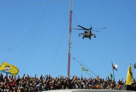 Kurds wave flags as a medevac helicopter from the US-led coalition flies over the site of Turkish air strikes near Al-Malikiyah on April 25, 2017
