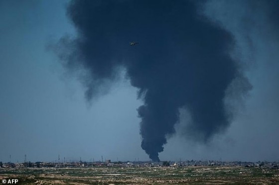 An Iraqi forces helicopter flies in front of black smoke rising from the horizon in west Mosul on April 25, 2017