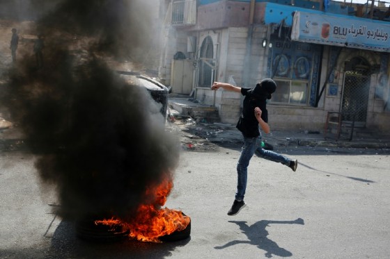 A masked Palestinian throws a stone towards Israeli troops during a protest on May 22, 2017 in support of prisoners on hunger strike in Israeli jails for more than a month and denouncing a visit by US President Donald Trump