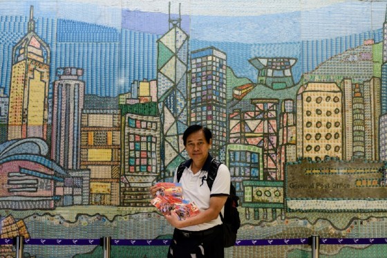 Stamp collector Vincent Lian, 62, poses in front of a mural made from stamps as he holds military-themed postacards that he printed