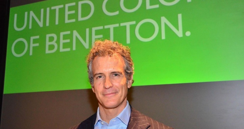 Alessandro Benetton posa sorridente accanto al logo dell'azienda